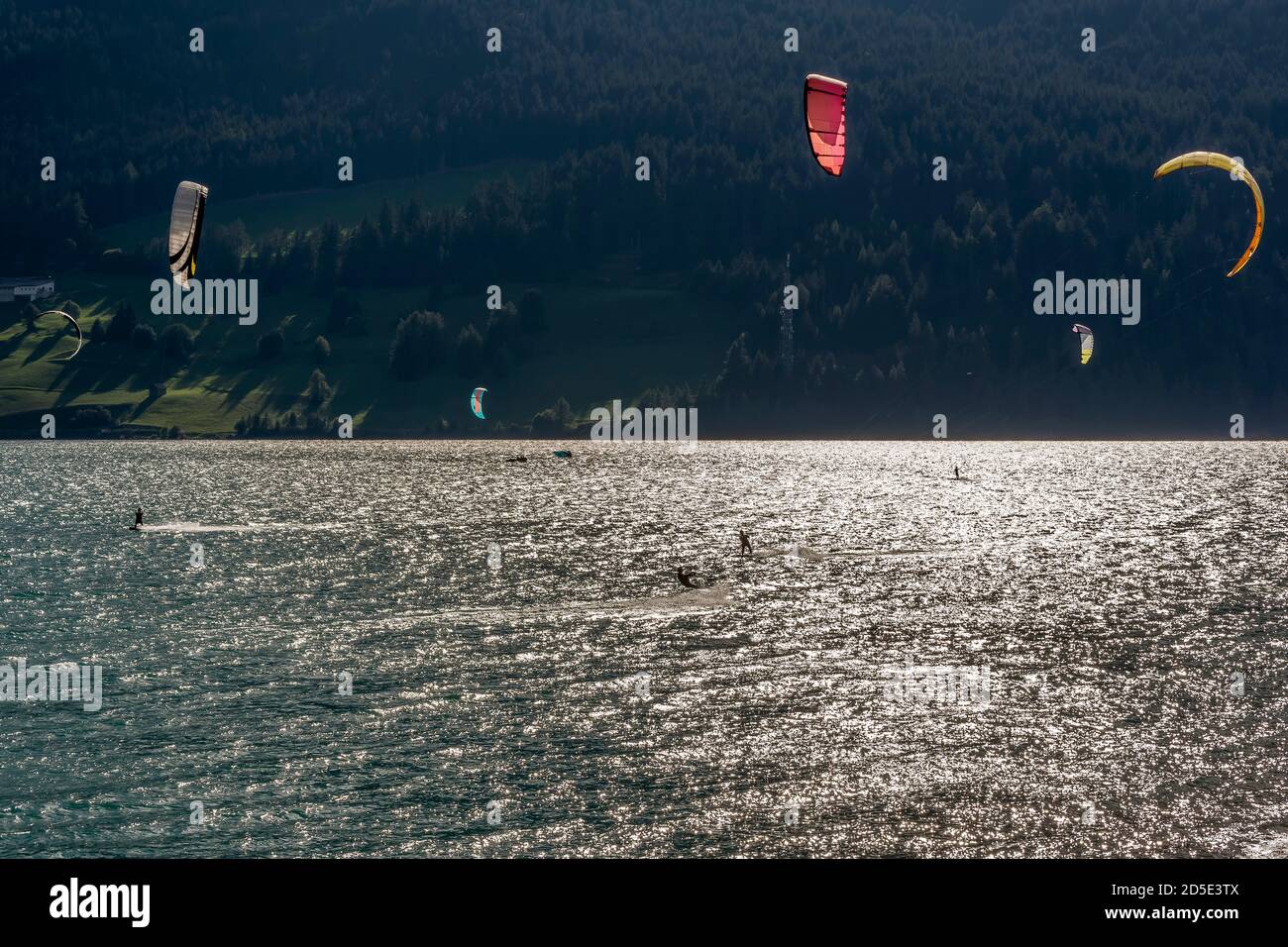 Diversi kite surfisti in azione sul Lago di Resia hanno girato contro la luce a Curon Venosta, Alto Adige, Italia Foto Stock