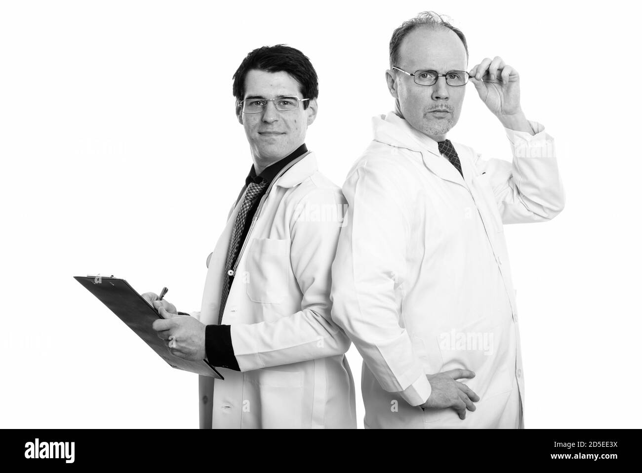 Uomo maturo medico tenendo occhiali con il giovane medico iscritto negli appunti sul dorso a dorso Foto Stock