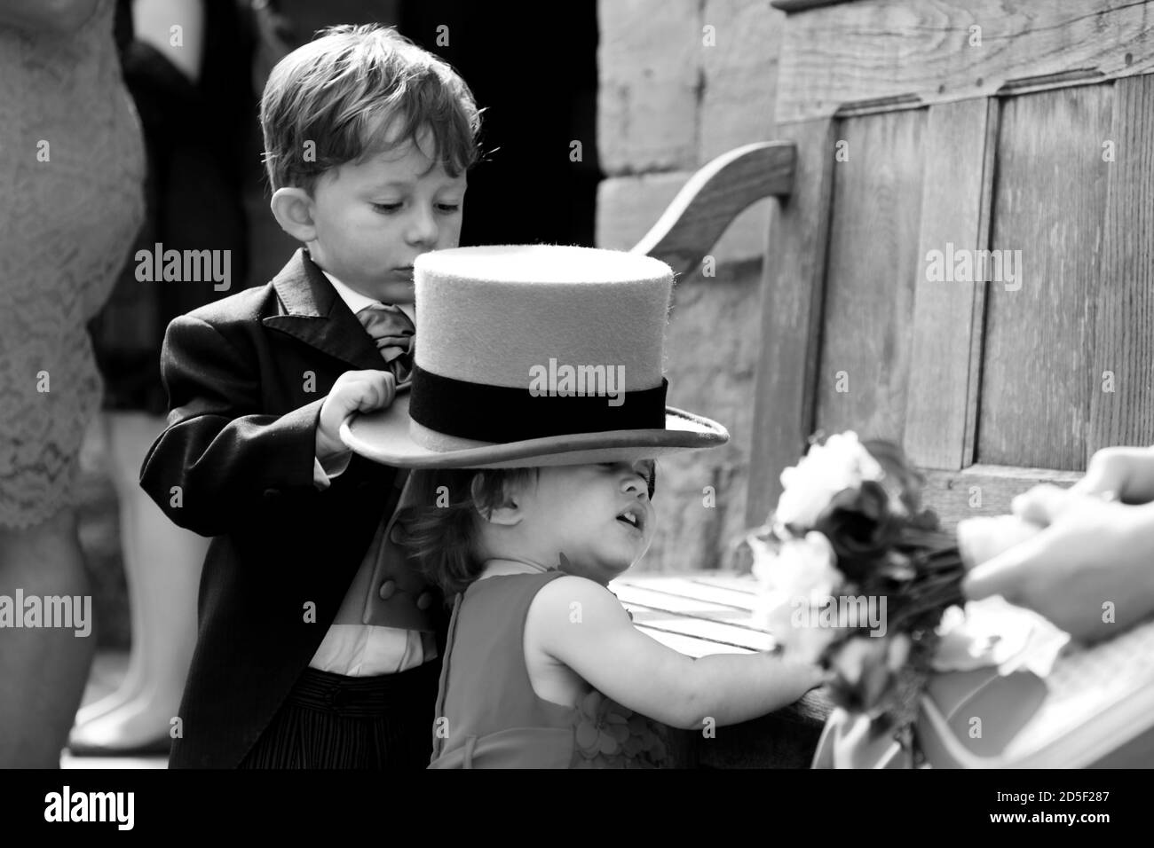Il ragazzo di pagina di nozze 4-5 anni mette il cappello di cima grigio sulla bambina. Simpatico e divertente fratello e sorella momento. Foto Stock