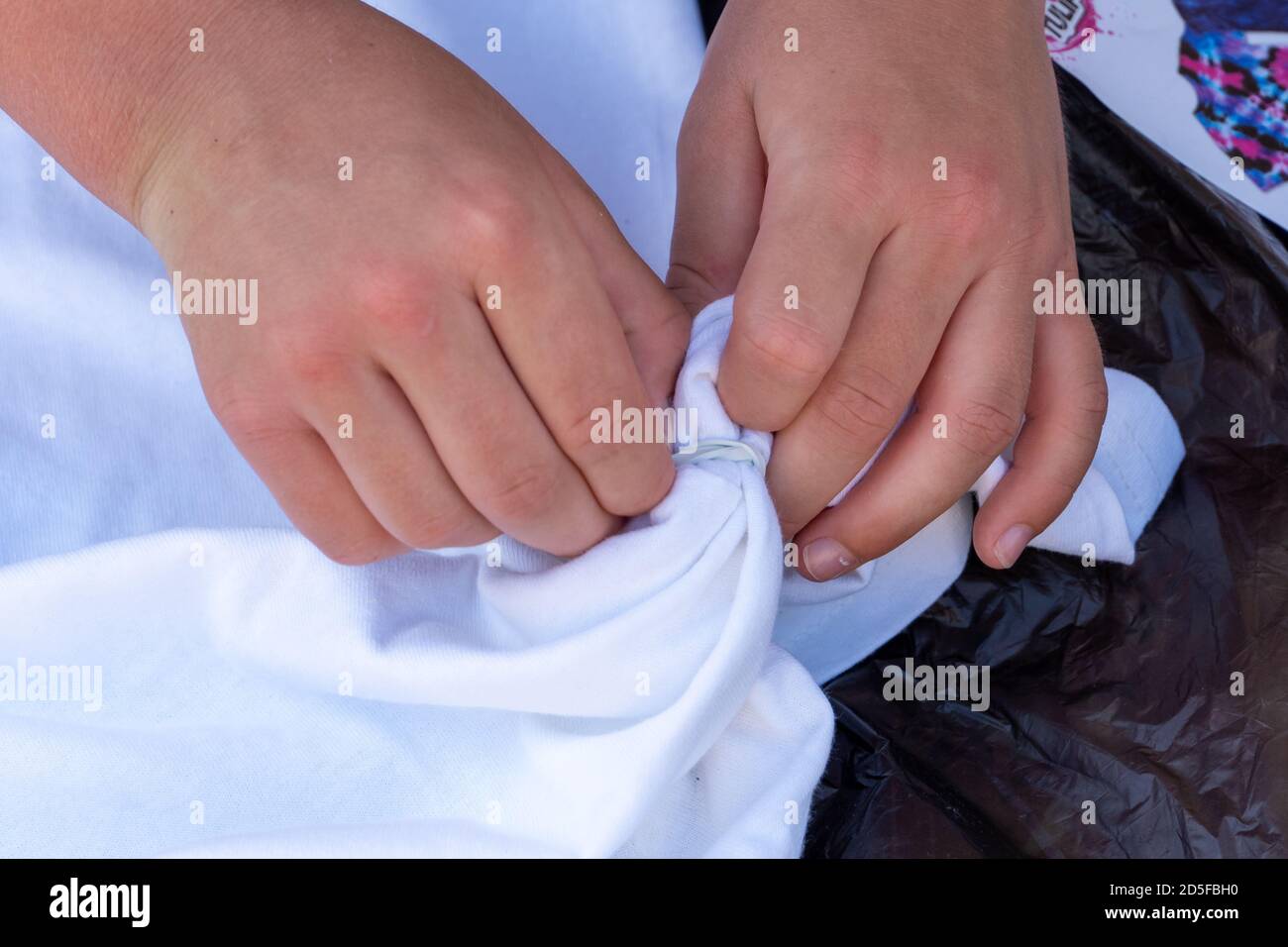 Mani del bambino che mettono insieme il tessuto bianco per un progetto creativo artistico di tintura di cravatta o concetti di cucitura. Vista dall'alto Foto Stock