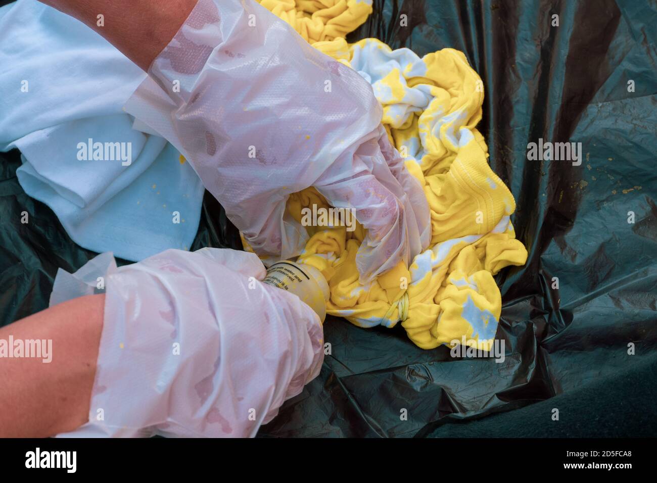 Lancette per bambini tie dye mani che mettono il dado giallo su una camicia bianca per i concetti artistici creativi. Foto Stock