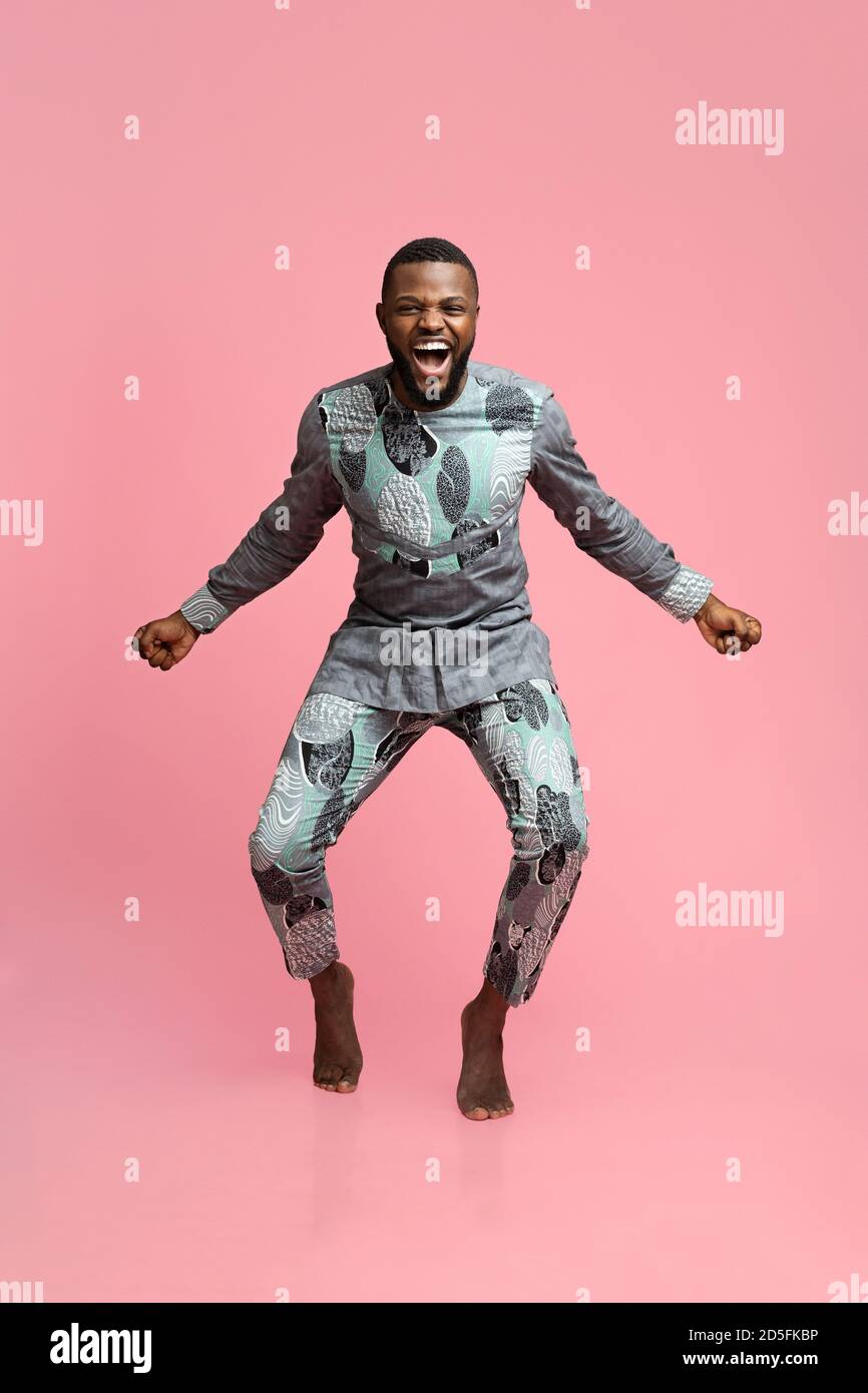 Un ragazzo nero emozionale in costume africano che danzano su sfondo rosa Foto Stock