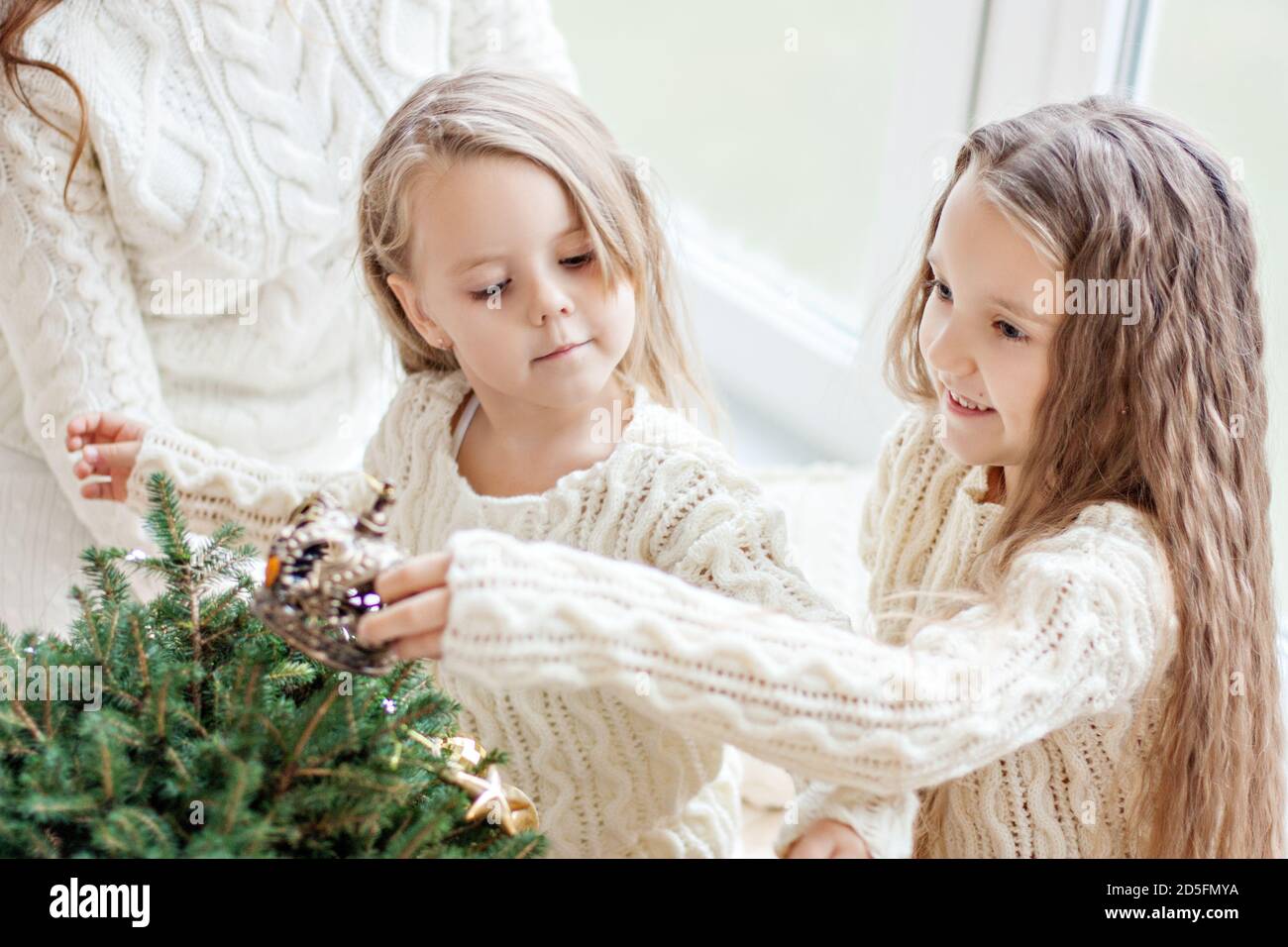 Due fidanzate della sorella bionda in maglia bianca pullover E calze stanno giocando dalla finestra panoramica con Natale alberi in attesa Foto Stock