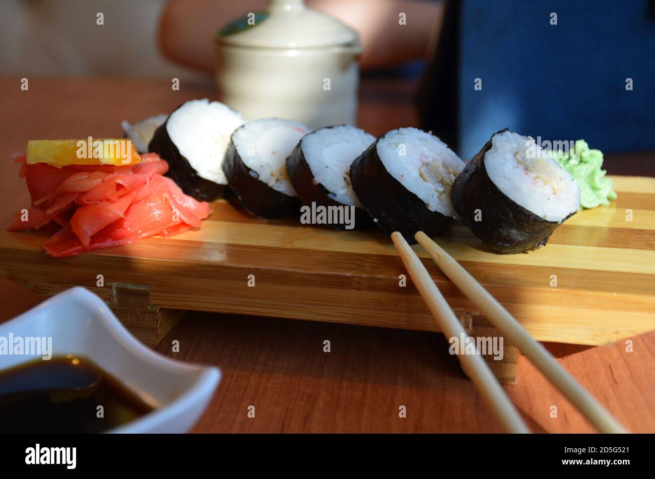 Involtini di salmone e caviale serviti su un piatto di sushi panini su un tavolo in un ristorante su uno stand di legno con bastoncini di pollo. Con salsa di soia, zenzero rosso e. Foto Stock