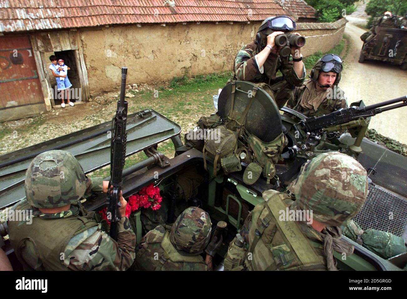 I Marines DEGLI STATI UNITI sono in allerta, in quanto la loro pattuglia in  veicoli blindati leggeri (LAV) si ferma in un villaggio albanese kosovaro  15 giugno. Una giovane albanese tiene il