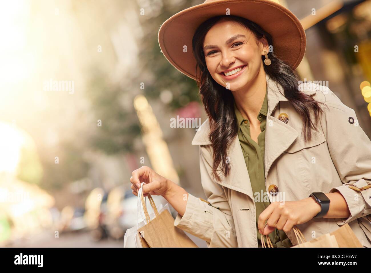 Visita boutique di moda. Ritratto di una giovane donna eccitata che indossa cappotto e cappello grigio con borse per lo shopping, in piedi sulla strada della città e sorridente. Shopaholic, moda, concetto di stile di vita della gente Foto Stock