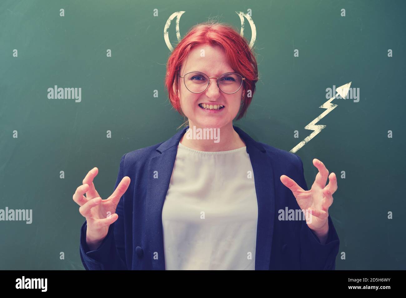 Insegnante di donna con una faccia malvagia e coda diabolica disegnata con gesso e corna. Arrabbiato insegnante di scuola su sfondo lavagna, Halloween Foto Stock