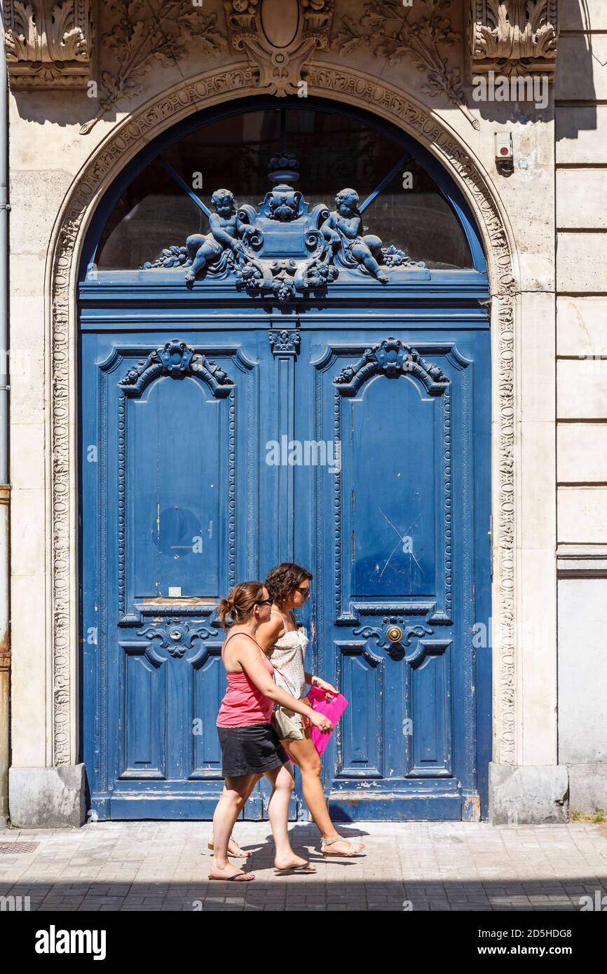 LILLE, FRANCIA - 19 luglio 2013. Due giovani donne passano una vecchia porta blu sbiadita in una porta ad arco, la scena di via Lille Foto Stock