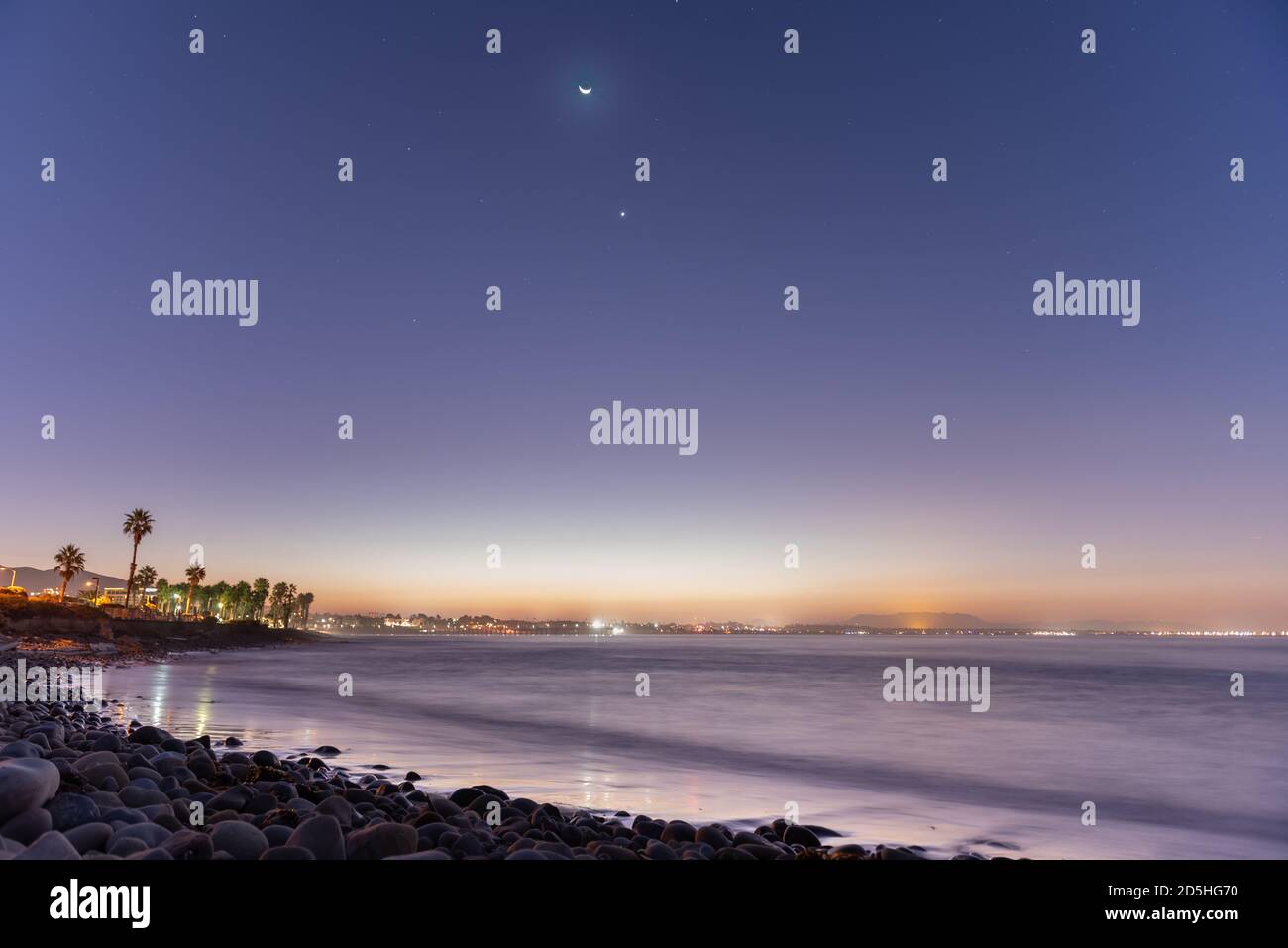 Luna pendente con Venere e stelle di costellazione che illuminano il cielo mentre l'alba si rompe sopra la pausa surf point. Foto Stock
