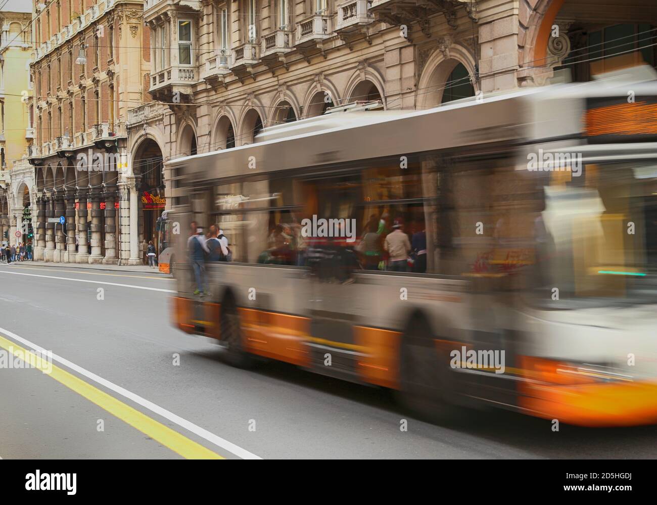 Movimento sfocato di autobus urbano arancione che viaggia su una strada principale in un contesto urbano con case storiche e galleria in background. XX Settembre Street in Foto Stock