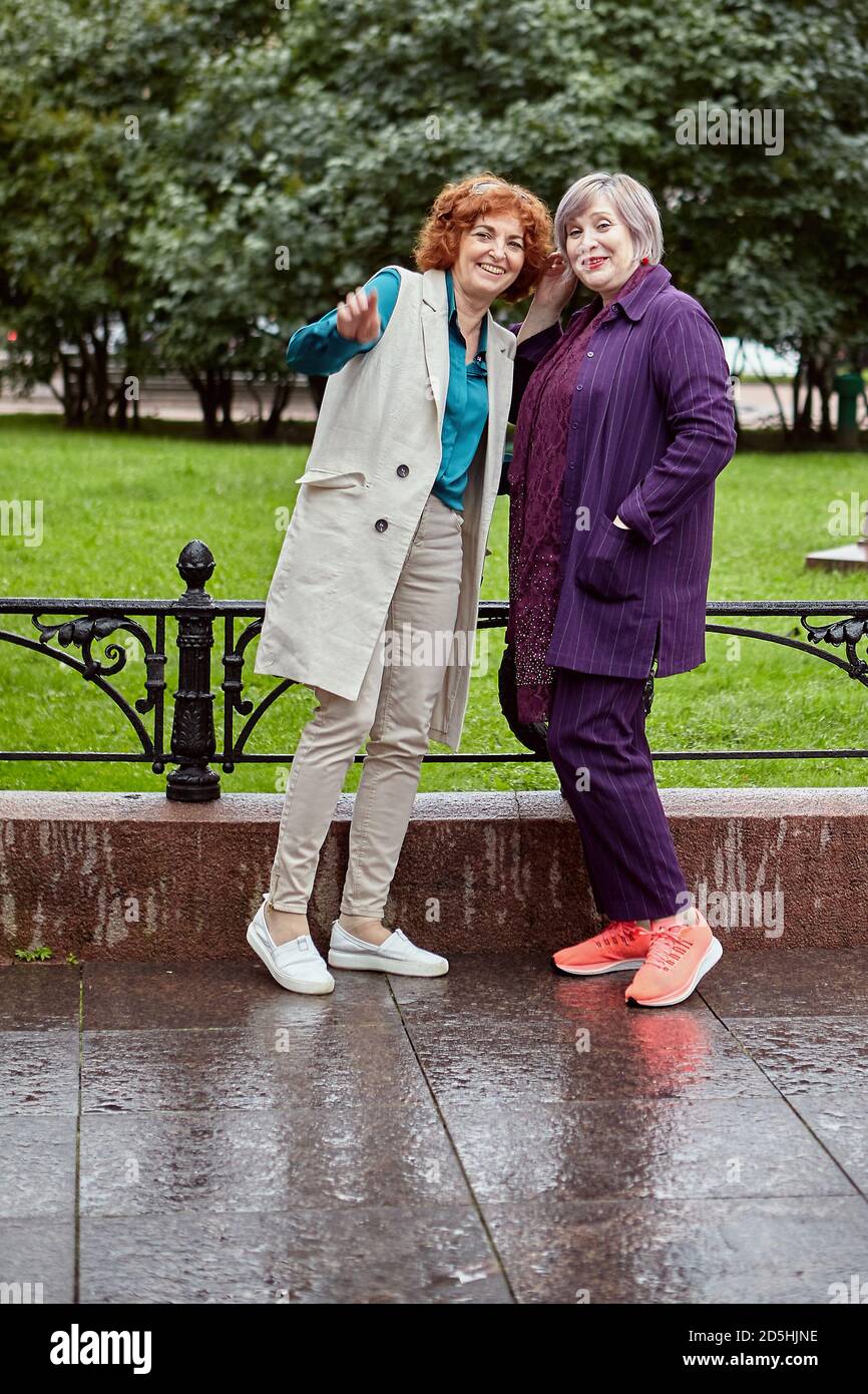 Due donne europee mature pettegolezzo su qualcosa in un parco cittadino in tempo piovoso. Foto Stock