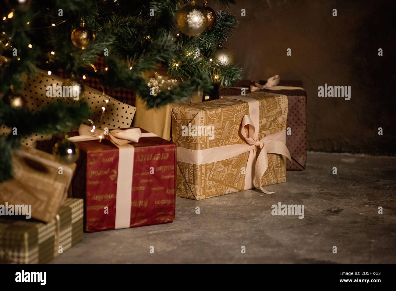 Biglietto di auguri per il nuovo anno. Sotto l'albero di Natale si trovano scatole di regali, avvolti in oro festivo, carta borgogna, legato con nastri. Spazio di copia. Bokeh vigilia Foto Stock