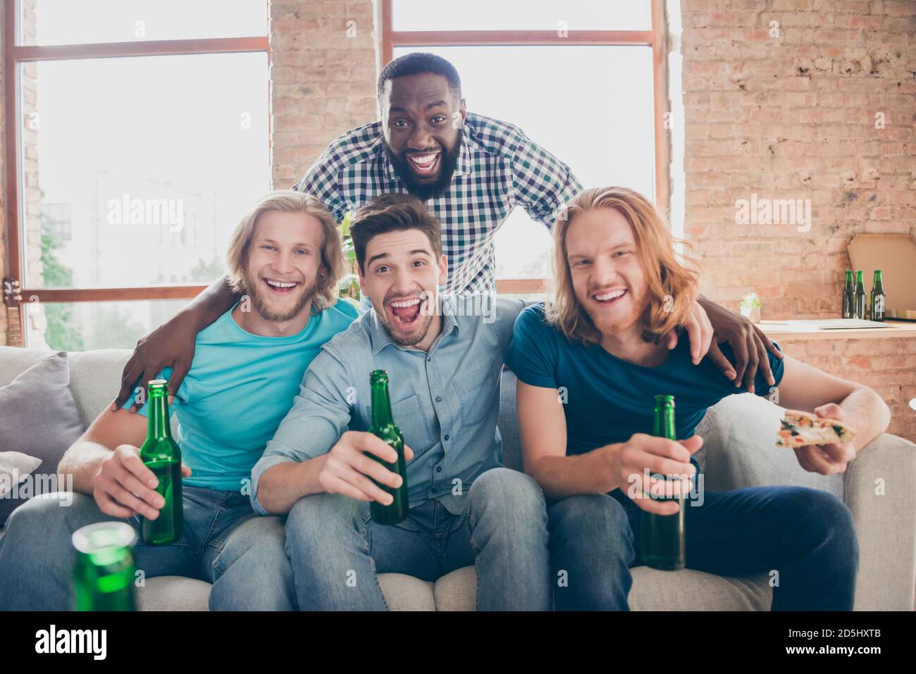 Quattro persone migliori amici uomini sedersi divano tenere pint bevanda bottiglia goditi il tempo libero guardando film hold pizza fetta in casa al chiuso Foto Stock