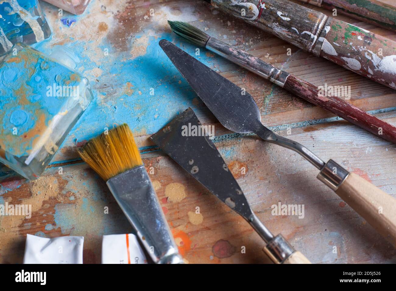 Scrivania artista e materials. Spazzole varie e coltelli pallete. La scrivania in legno è coperta con belle diverse vernici colorate. Foto Stock