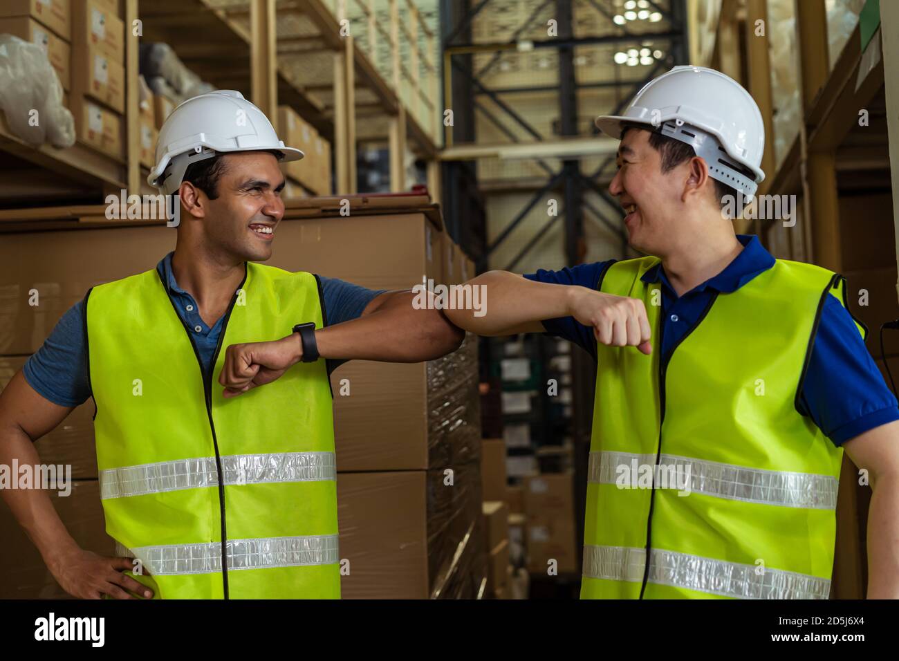 I lavoratori di magazzino di fabbrica maschi che fanno il gomito che lavora nel settore logistico indoor. Amici saluto e scuotere con gomiti come nuovo normale dopo Covid-19 Foto Stock