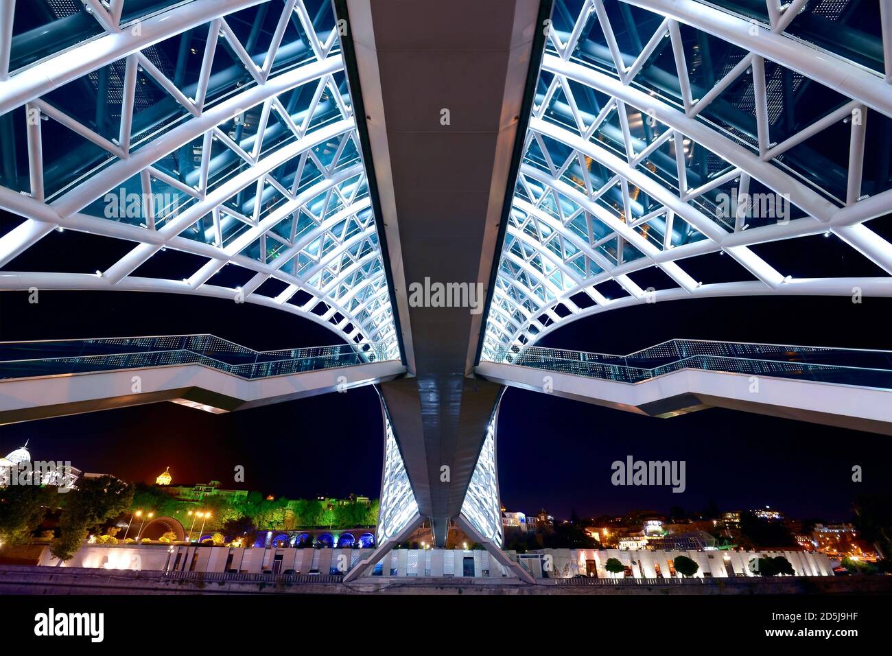 Ponte della Pace di notte a Tbilisi, Georgia. Ponte pedonale dal design moderno che attraversa il fiume Kura. Design simmetrico con scale. Foto Stock