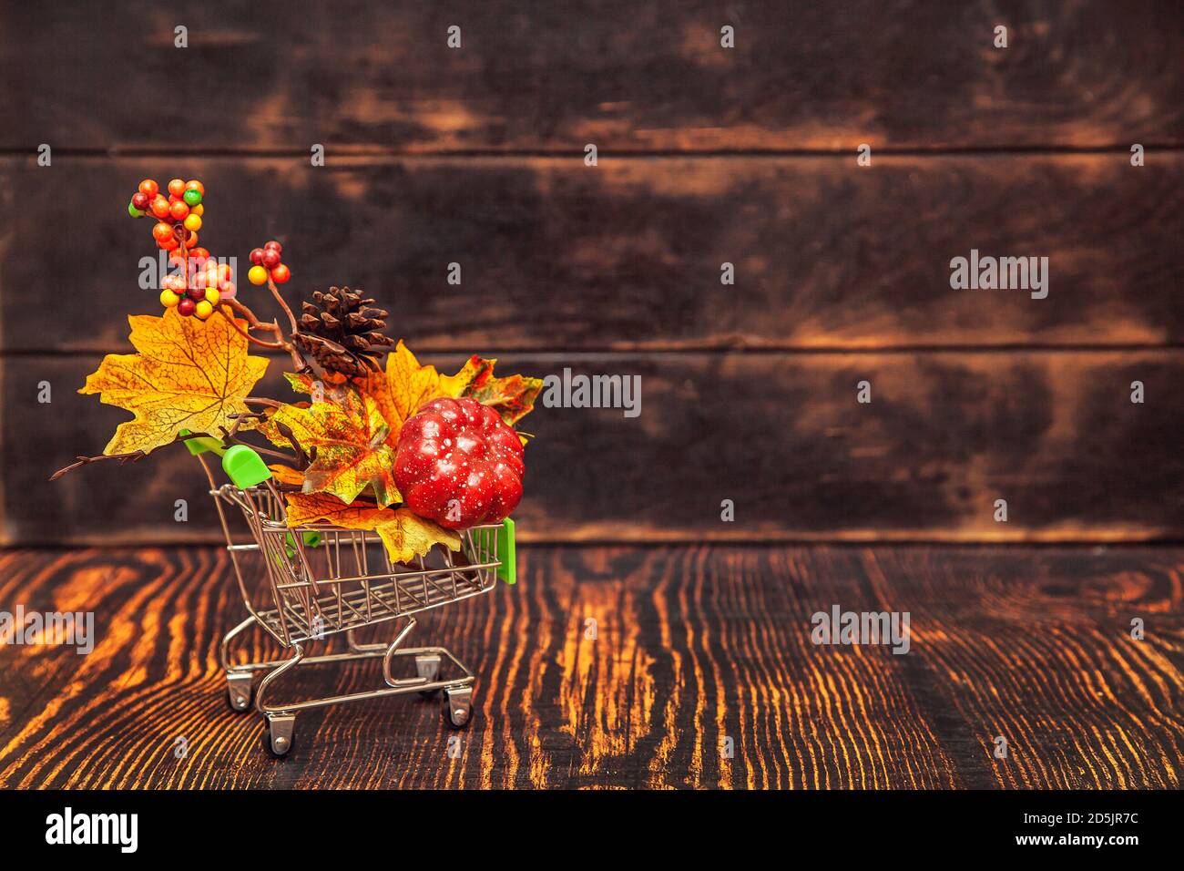 Vendita autunnale. Carrello su sfondo di legno con decorazione autunnale - foglie di acero, coni, bacche, zucca. Foto Stock