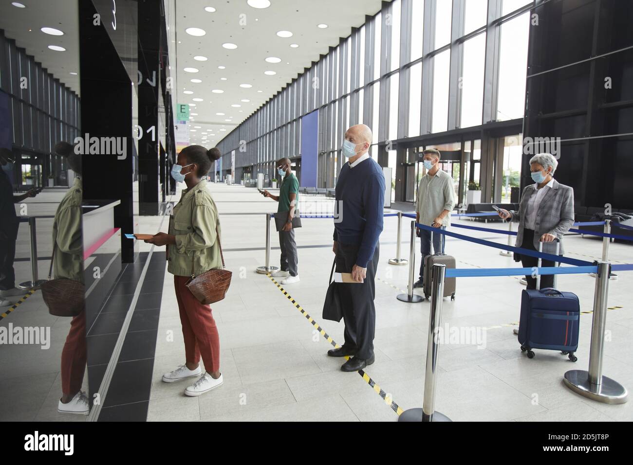 Gruppo di persone in maschere protettive persone che mantengono il sociale distanza all'aeroporto mentre si è in fila Foto Stock