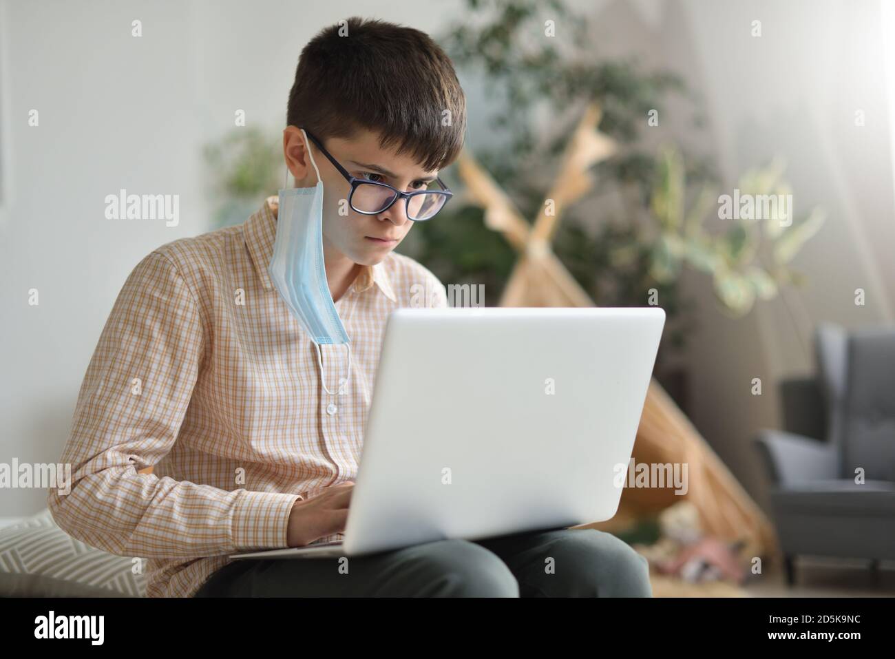 Teen boy toglie la sua maschera protettiva e impara a distanza da un computer portatile Foto Stock
