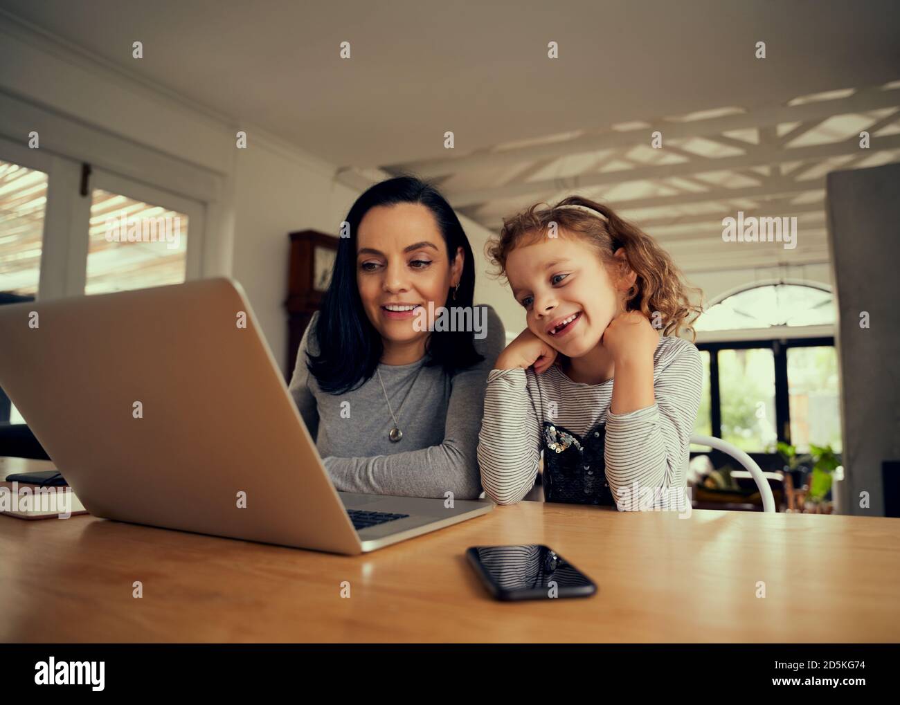 Donna allegra con figlia prescolare che guarda video divertenti sul laptop a casa Foto Stock