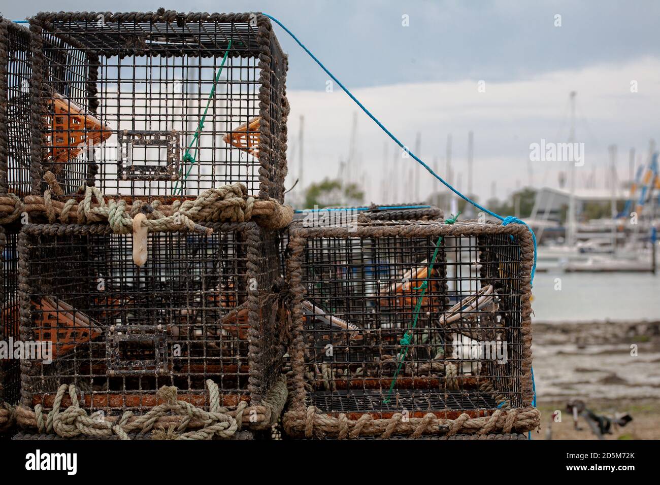 Pentole di aragosta legate insieme sulla costa pronte per l'uso in una giornata grigia. Barche e porticciolo in terra posteriore. Pesca industria costa bassa marea. Foto Stock