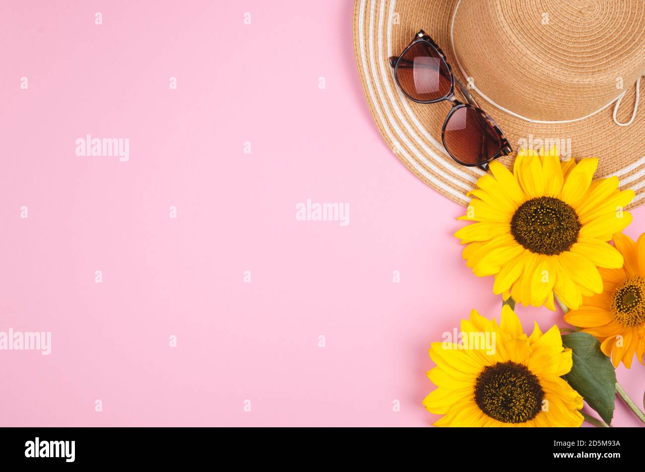 Flatlay con occhiali da sole, cappello di paglia e girasole giallo brillante su sfondo rosa Foto Stock