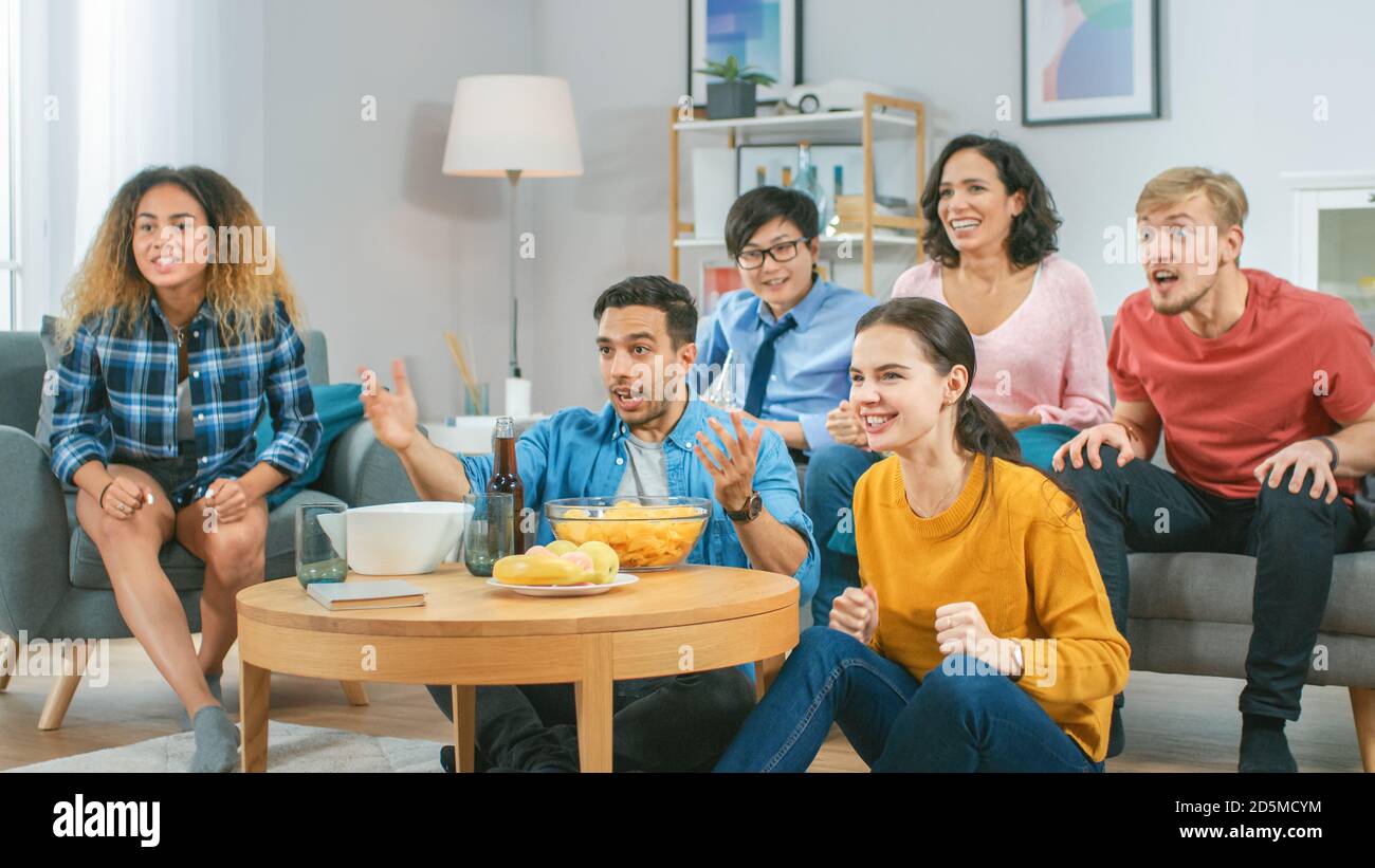 A casa diversi amici di gruppo guardare la TV insieme, mangiare snack e bere bevande. Probabilmente guardano il gioco di sport o film di divertimento. Foto Stock