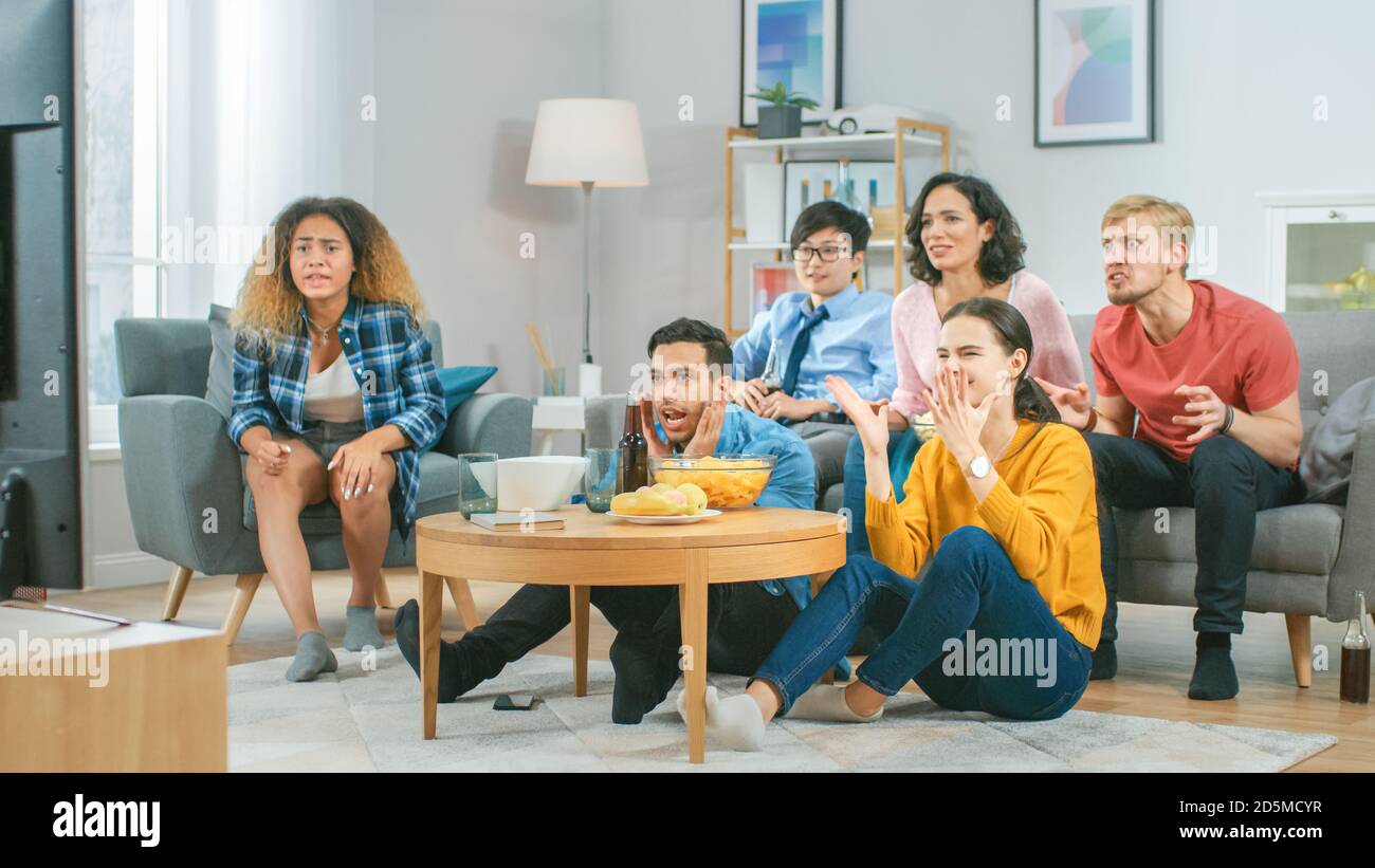 A casa diversi amici di gruppo guardare la TV insieme, mangiare snack e bere bevande. Probabilmente guardano il gioco di sport o film di divertimento. Foto Stock