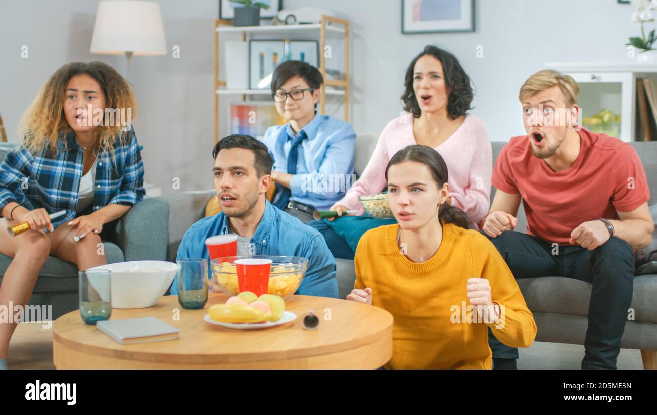 A casa diversi amici di gruppo guardare la TV insieme, mangiare snack e bere bevande. Probabilmente guardano il gioco di sport, film o sitcom TV Show Foto Stock