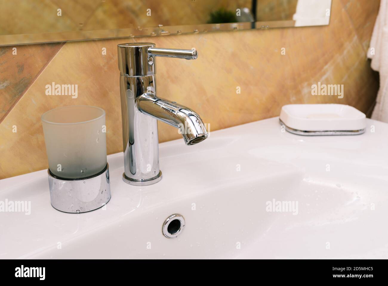 Rubinetto cromato e lavello bianco. Interno di un bagno in una casa o in un hotel. Il concetto di lavaggio delle mani e protezione dai virus Foto Stock