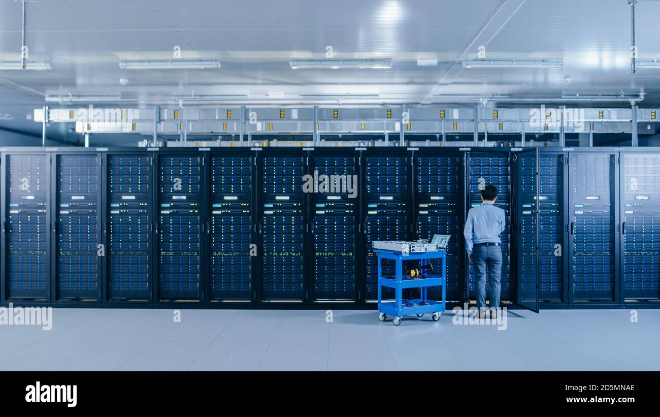 Nel data center: IL tecnico IT che lavora con i rack server lavora con il cabinet aperto per installare il nuovo hardware per l'aggiornamento del sistema, il carrello si trova accanto a. Foto Stock