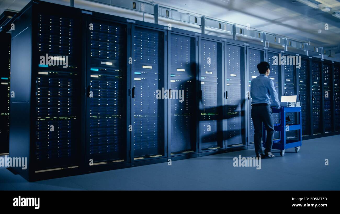 Nel moderno data center: Tecnico IT che esegue la manutenzione e la diagnostica. Spinge il carrello accanto ai rack server. Aggiornamento pianificato delle apparecchiature di sistema e. Foto Stock