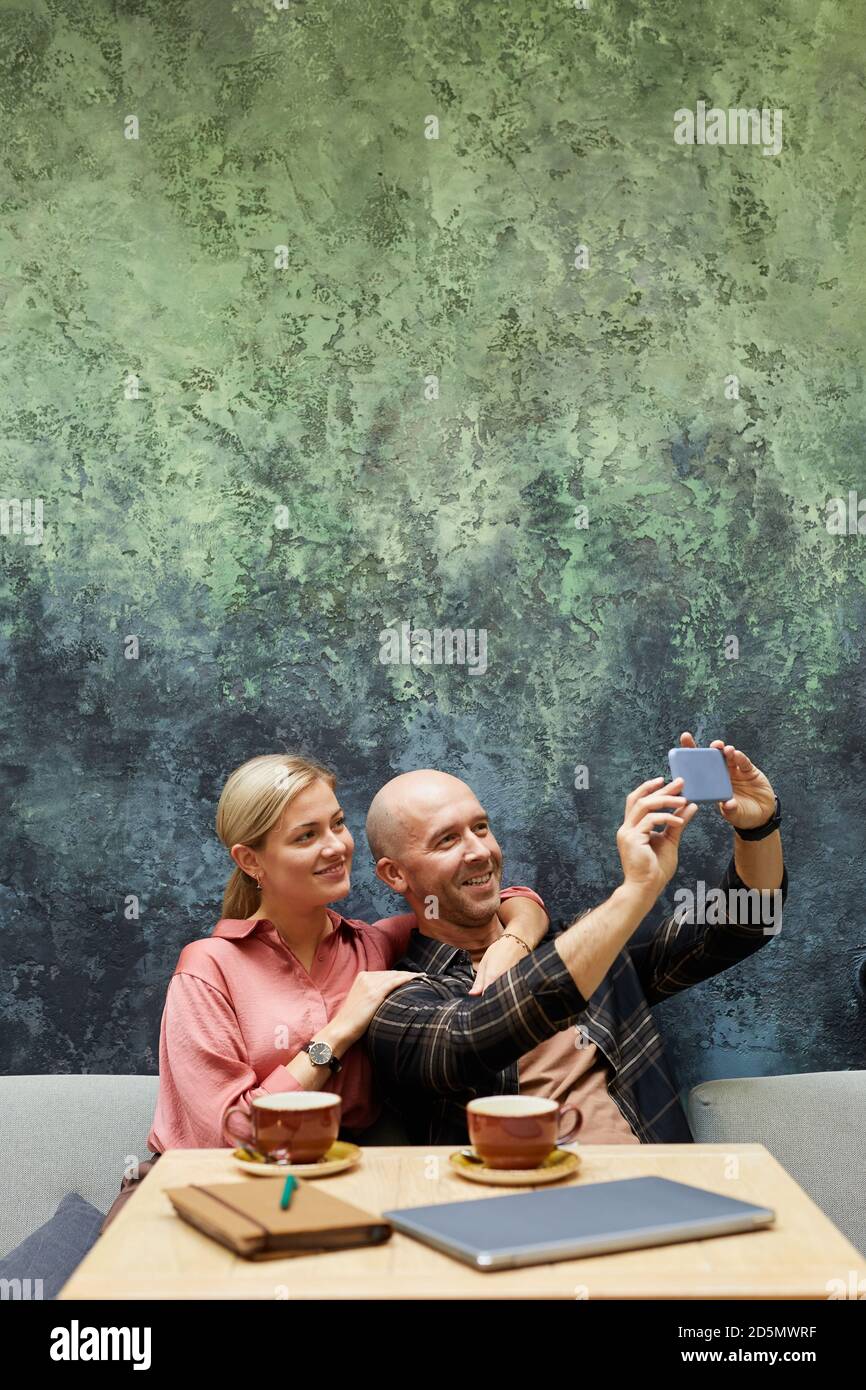 Uomo sorridente che fa ritratto selfie sul telefono cellulare con la sua ragazza durante il loro tempo in caffetteria Foto Stock