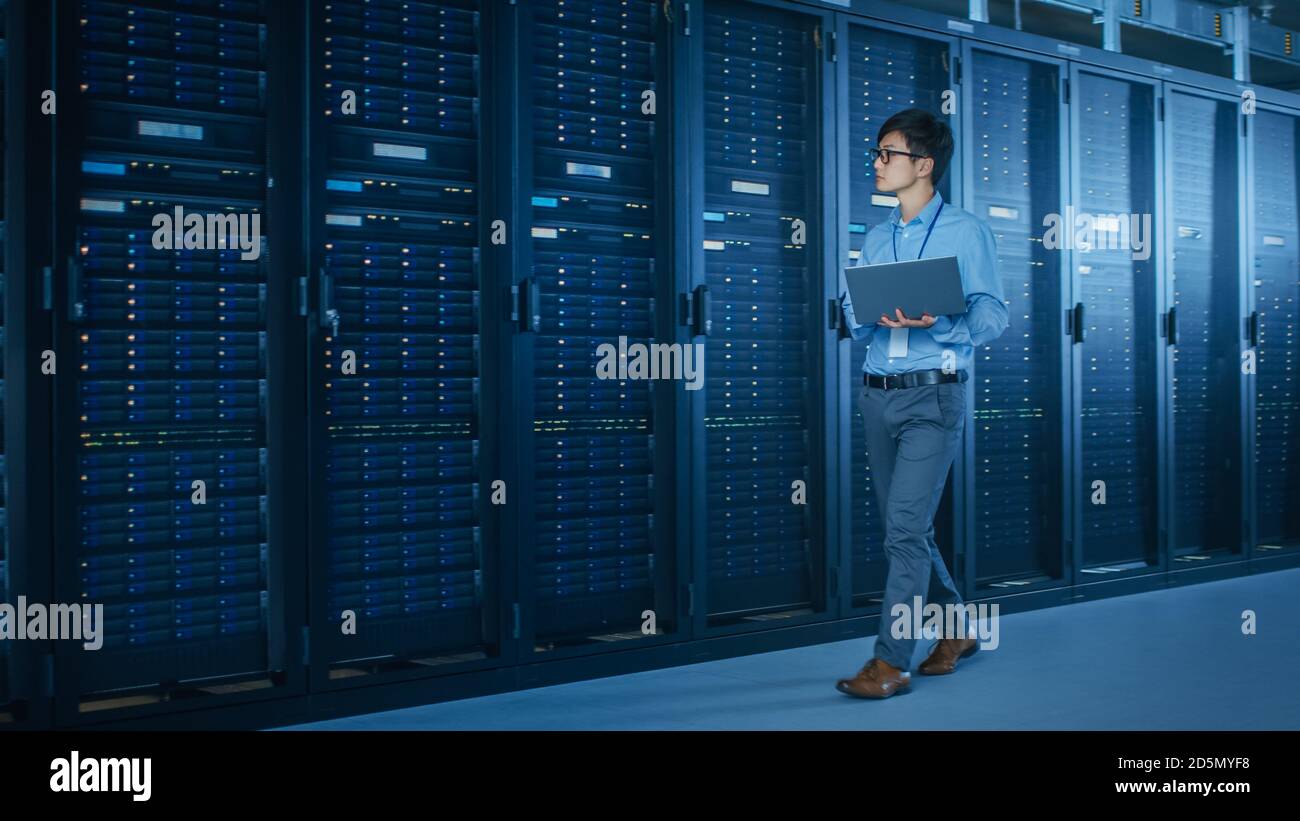 Nel moderno data center: Il tecnico IT che lavora con i rack server utilizza il notebook per la manutenzione e la diagnostica. Controllo della stabilità del sistema Foto Stock