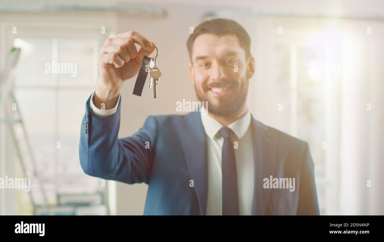 Agente immobiliare di successo in una tuta sorride e offre le chiavi da un nuovo appartamento. Spaziosa Nuova casa in vendita da Professional Real Estate Broker Foto Stock