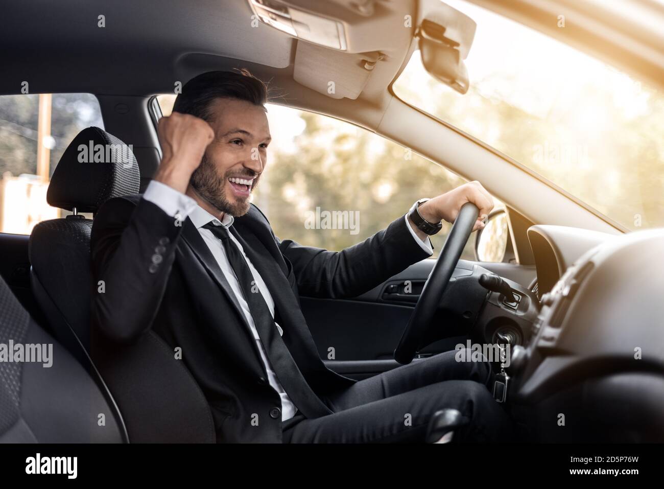 Uomo d'affari di media età che festeggia il successo durante la guida dell'auto Foto Stock