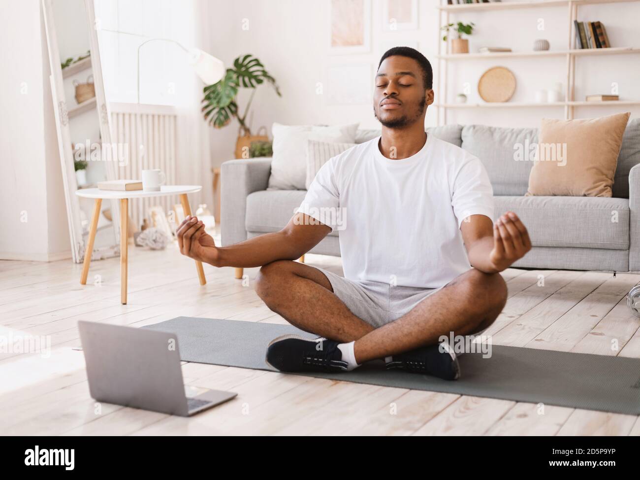Black Man meditando facendo Yoga seduto al laptop a casa Foto Stock