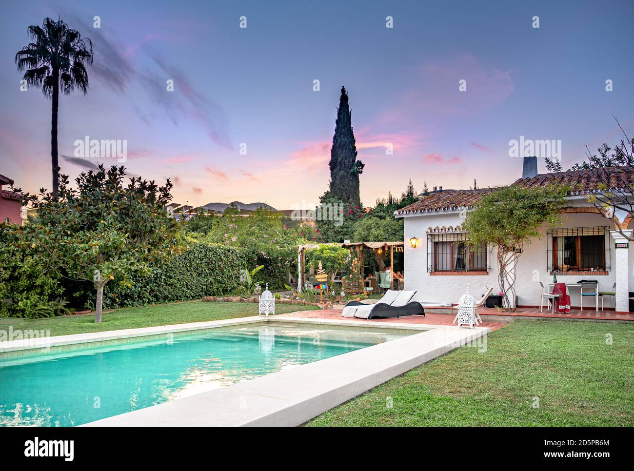 Tramonto in una rilassante villa vacanza con piscina con solarium, piscina con sedie, ombrellone, erba, giardino, portico e gazebo. Foto Stock