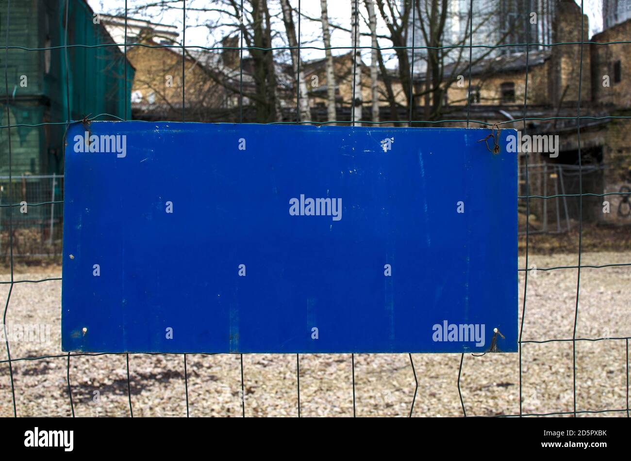 Cartello blu vuoto che indica la presenza di una recinzione. Firmare sulla recinzione del filo. Vecchio edificio sullo sfondo. Cartello con spazio per la copia. Rettangolo blu. Segnale stradale. Foto Stock