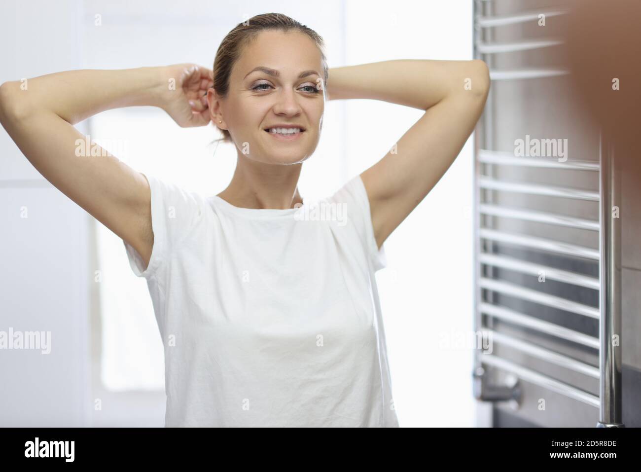 Donna in T-shirt bianca si erge di fronte allo specchio del bagno e sorride. Foto Stock