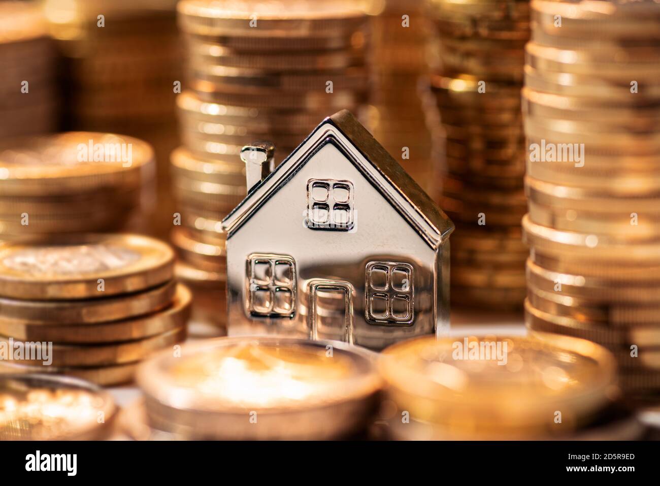 Piccola casa color argento tra pile di monete Foto Stock