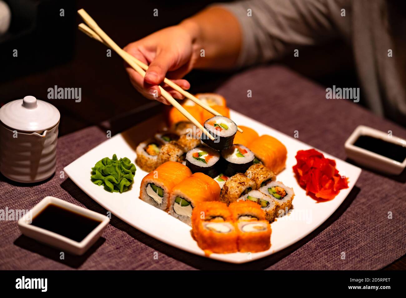 Persona che mangia sushi con chopsticks nel ristorante. Crop persona anonima con chopsticks mangiare vari tipi di sushi panini serviti con wasabi e. Foto Stock