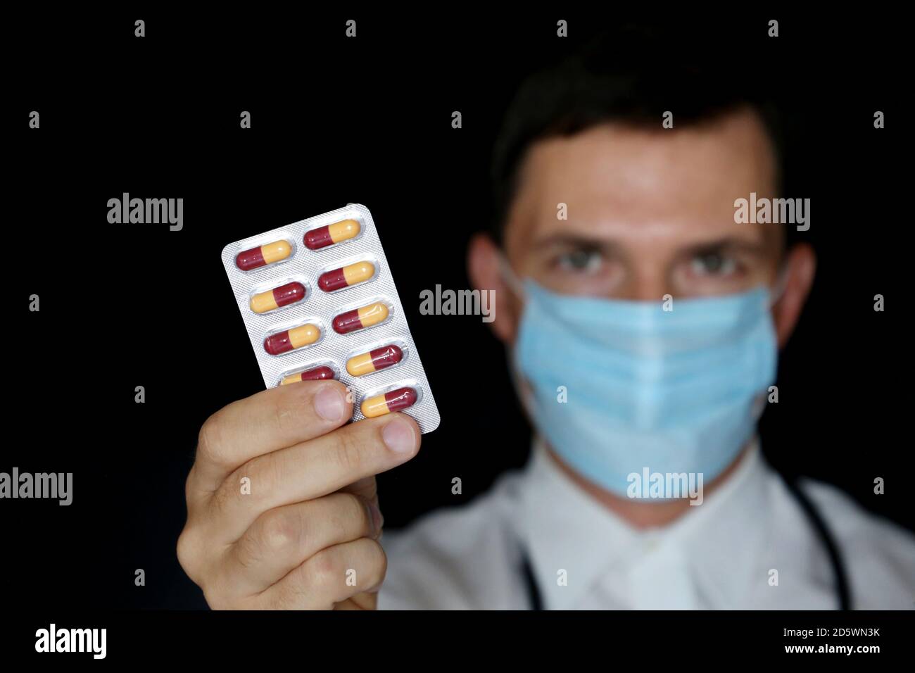 Medico in maschera medica contenente blister confezione di pillole, mano maschile con farmaco primo piano. Concetto di farmacista, farmaci, antibiotici o vitamine Foto Stock
