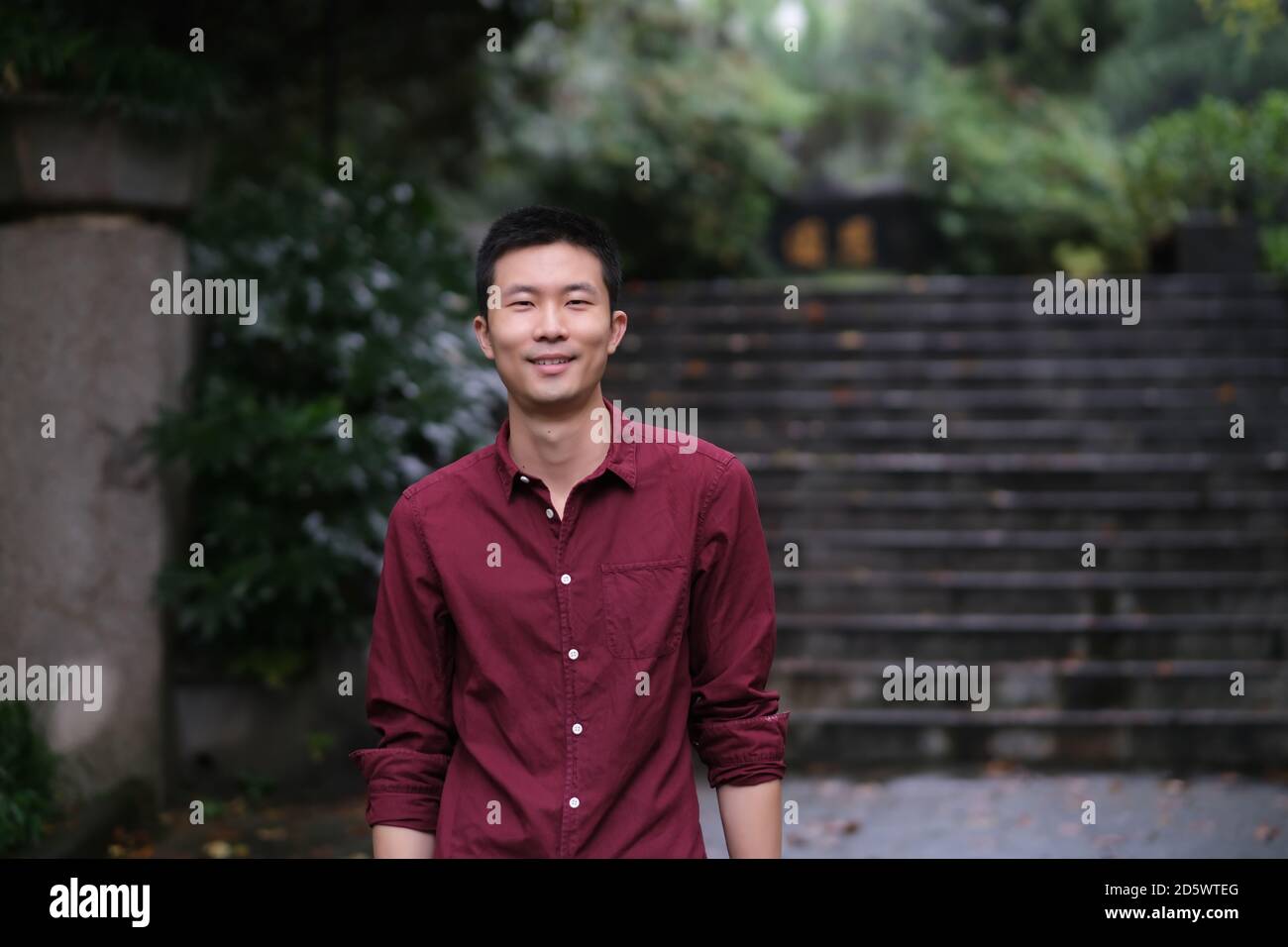 Scatto medio di un giovane asiatico sorridente che guarda la macchina fotografica. Nel parco naturale Foto Stock