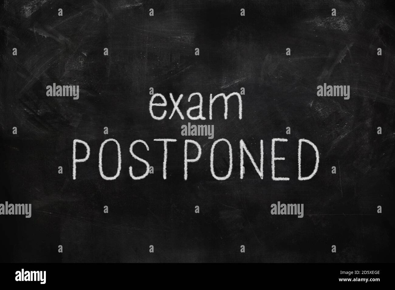 Exam postponed written with white and red chalk on blackboard in classroom Foto Stock
