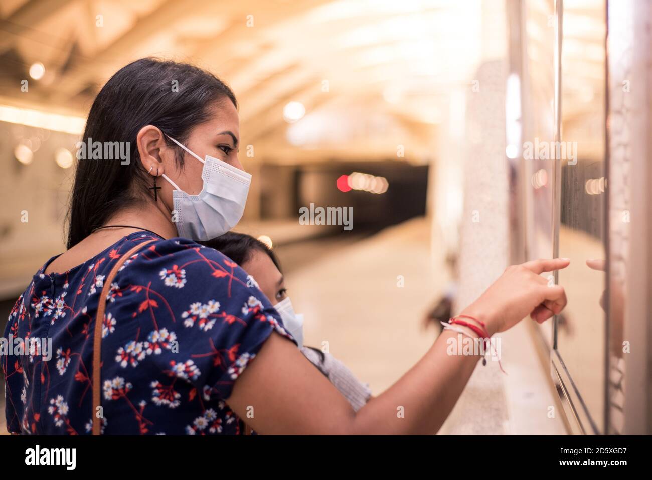 Giovane madre che indica e mostra la figlia sulla mappa dove stanno andando andare. Concetto di trasporto nella nuova normalità con maschere mediche. Foto Stock