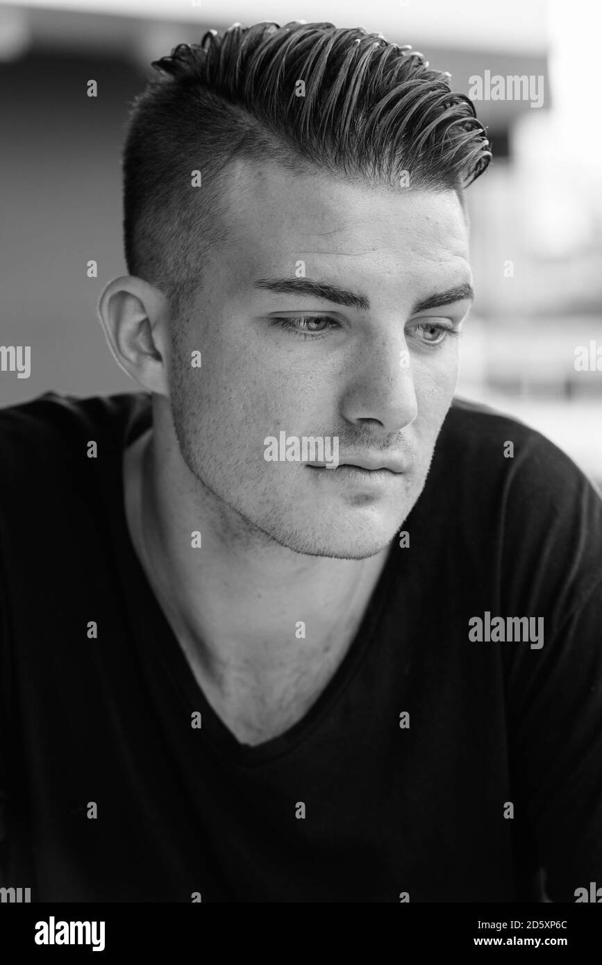 Giovane uomo bello guardare verso il basso mentre il pensiero al di fuori della caffetteria Foto Stock
