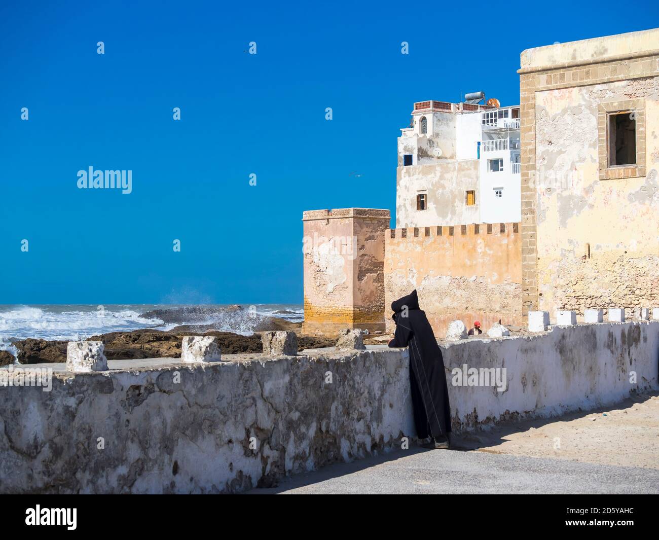 Marocco, Essaouira, Berber in djellaba nera alla parete del porto Foto Stock