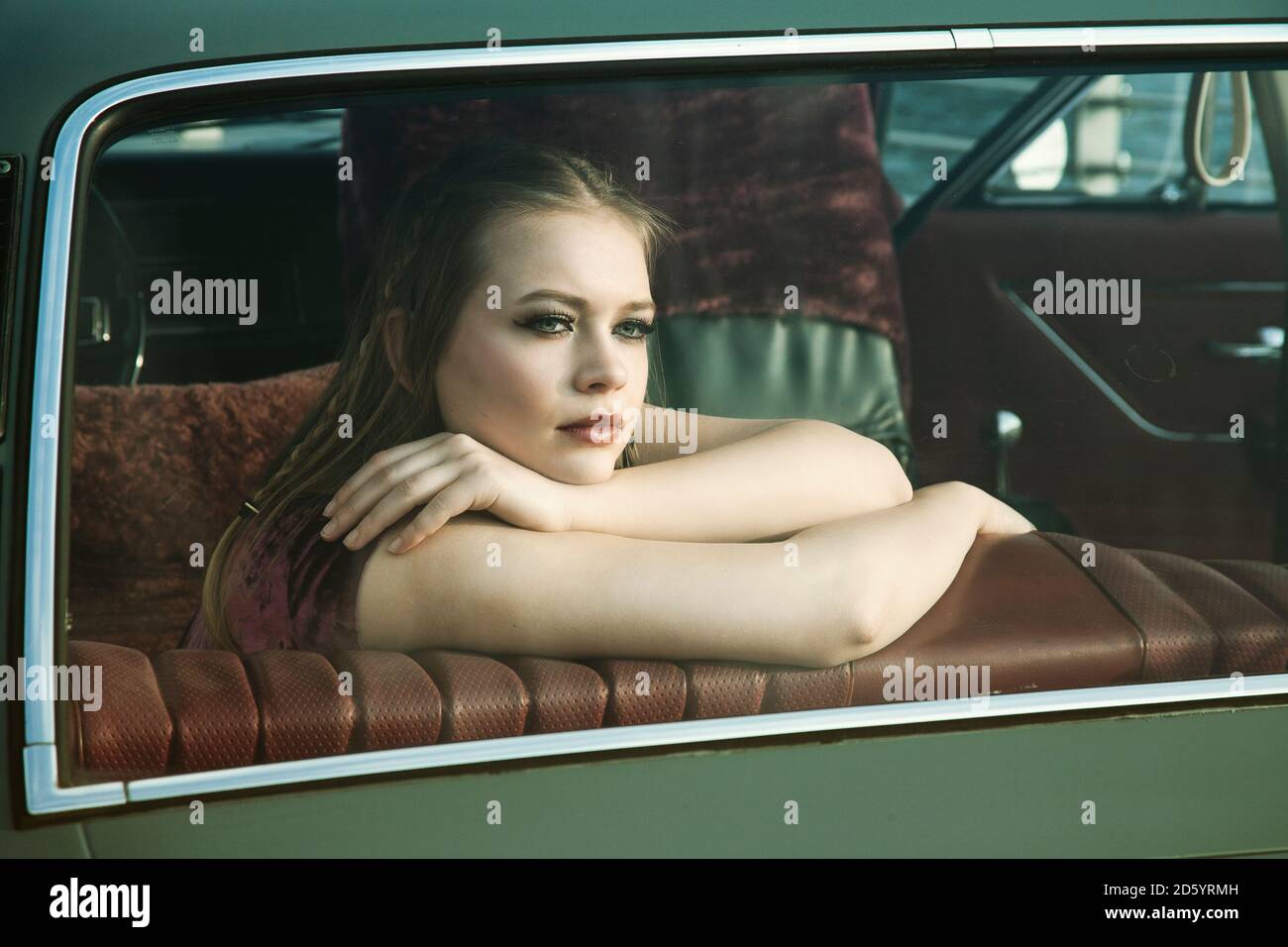 Ritratto di giovane donna che guarda attraverso il finestrino posteriore dell'auto d'epoca Foto Stock