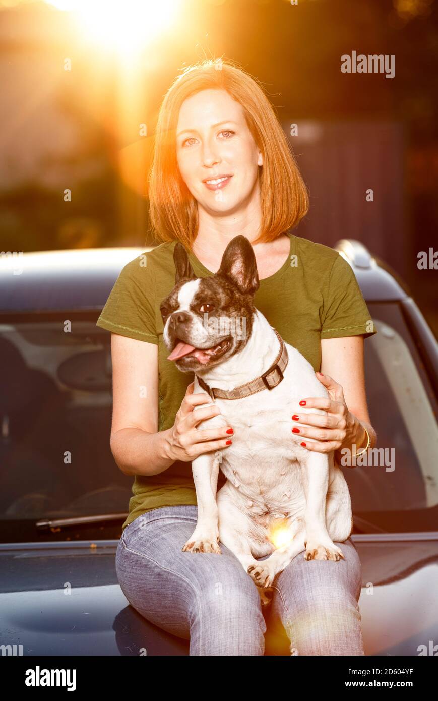 Ritratto di donna redheaded seduta sul cofano per auto con il suo bulldog francese Foto Stock